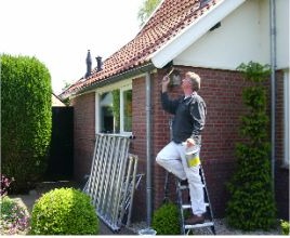 Schilder op een trap schildert de dakgoot van een bakstenen woning