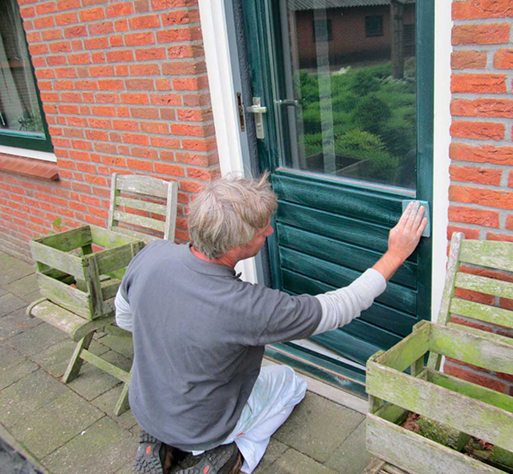 Schilder schuurt een groene voordeur voordat die opnieuw wordt geschilderd